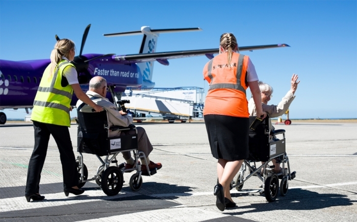 twee rolstoelgebruikers met Passengers with Restriced Mobility Assistance lopen naar vliegtuig