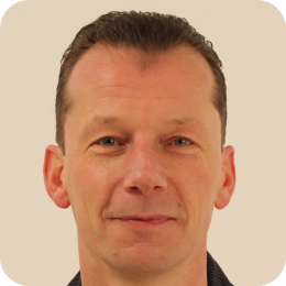 Portret van een man met kort, donker, terugwijkend haar, die recht in de camera kijkt.