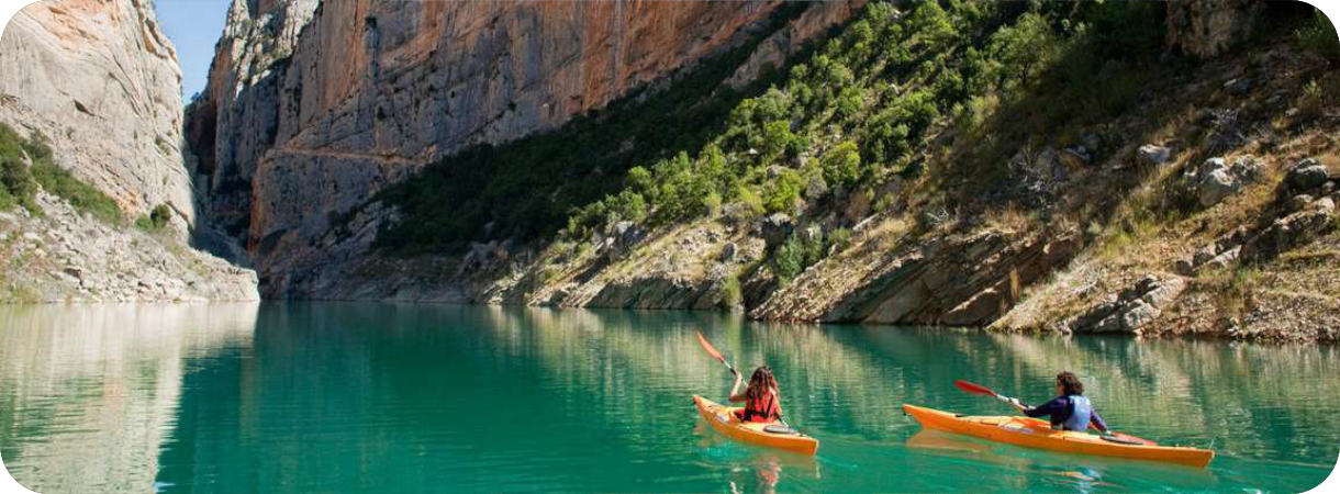 Twee personen kajakken op helder turquoise water in de smalle kloof van Congost de Mont-rebei met steile, hoge rotswanden