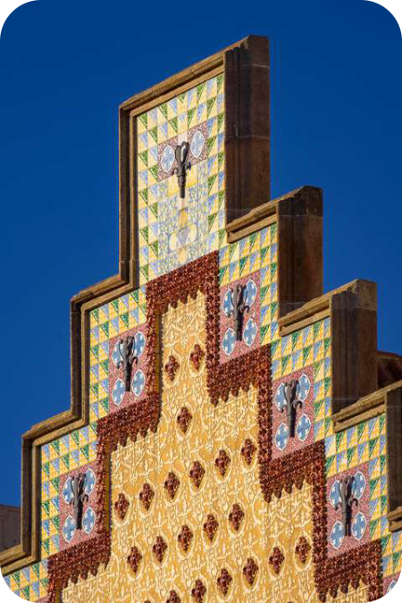Trapvormige geveltop van Casa Amatller in Barcelona met kleurrijke geometrische tegels tegen een blauwe lucht.