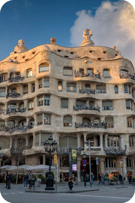 Vooraanzicht van Casa Milà (La Pedrera) in Barcelona, een golvend stenen gebouw ontworpen door Antoni Gaudí onder een deels bewolkte blauwe lucht