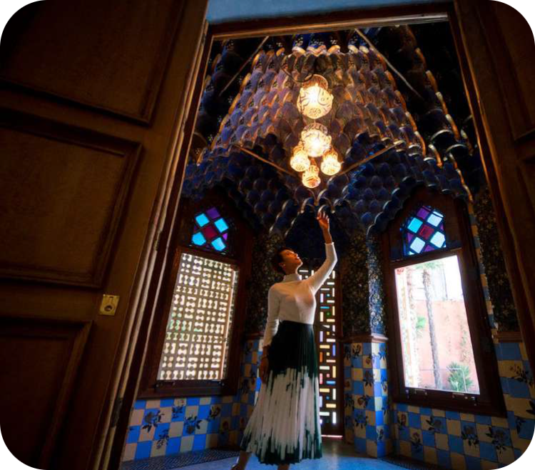 Een vrouw staat onder een blauw, oosters gewelfd plafond met goudkleurige lampen in de rookkamer van Casa Vicens.