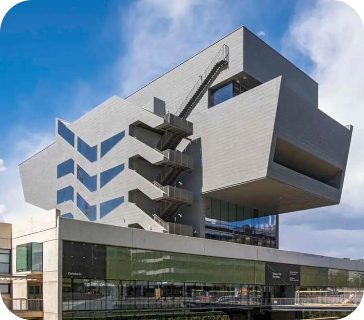 Modern, zilverkleurig museumgebouw met een ver uitstekende, asymmetrische bovenbouw en een opvallende buitentrap onder een blauwe lucht.
