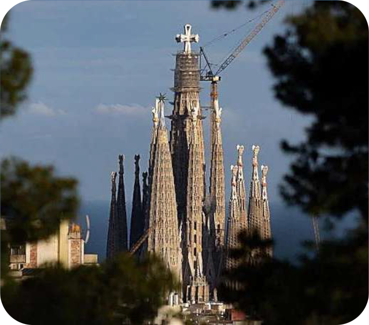 Afstandsblik op de Sagrada Família in Barcelona, met de focus op de centrale Toren van Jezus Christus inclusief een groot kruis op de top en een bouwkraan.