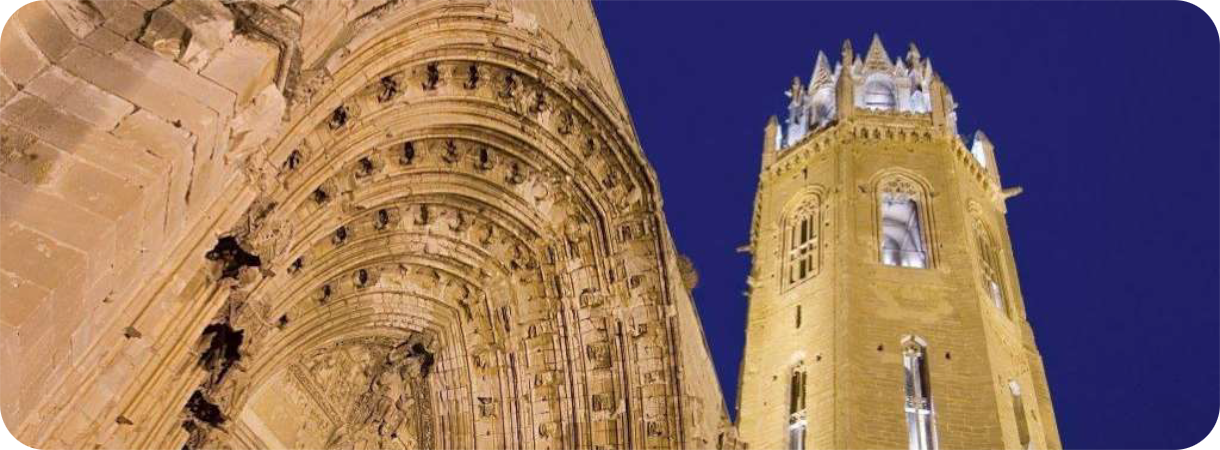 Verlichte gotische poort en de achthoekige klokkentoren van de La Seu Vella kathedraal in Lleida tegen een donkerblauwe avondlucht