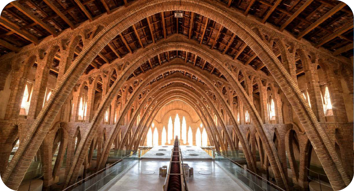 Interieur van de modernistische Catedral del Vi in Spanje met monumentale, gelaagde paraboolbogen van baksteen boven een wijnkelder.