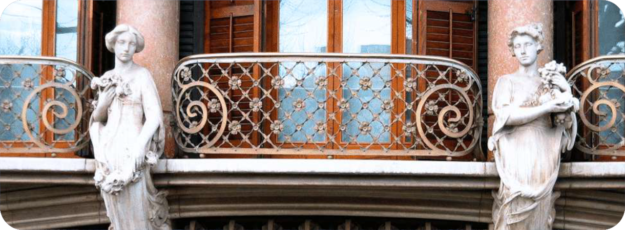 Smeedijzeren Art Nouveau-balkon geflankeerd door twee stenen kariatiden (vrouwenbeelden) aan de gevel van Casa Solà-Morales