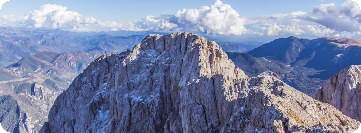 Panoramisch bovenaanzicht van de Pedraforca berg in Catalonië, Spanje, met de kenmerkende steile, ruige kalkstenen rotspunten die uitspreken tegen een achtergrond van glooiende bergen, diepe valleien en een blauwe lucht met witte wolken.