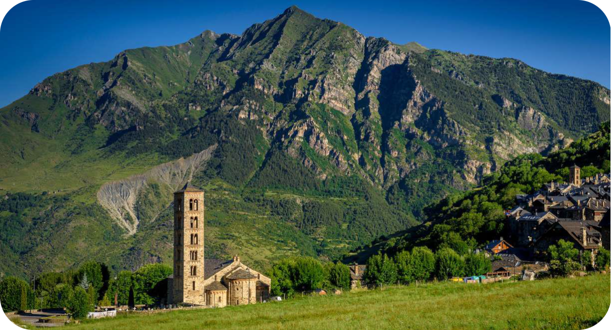 Een romaanse stenen kerk met een opvallend hoge, slanke klokkentoren in een groen berglandschap van de Pyreneeën.