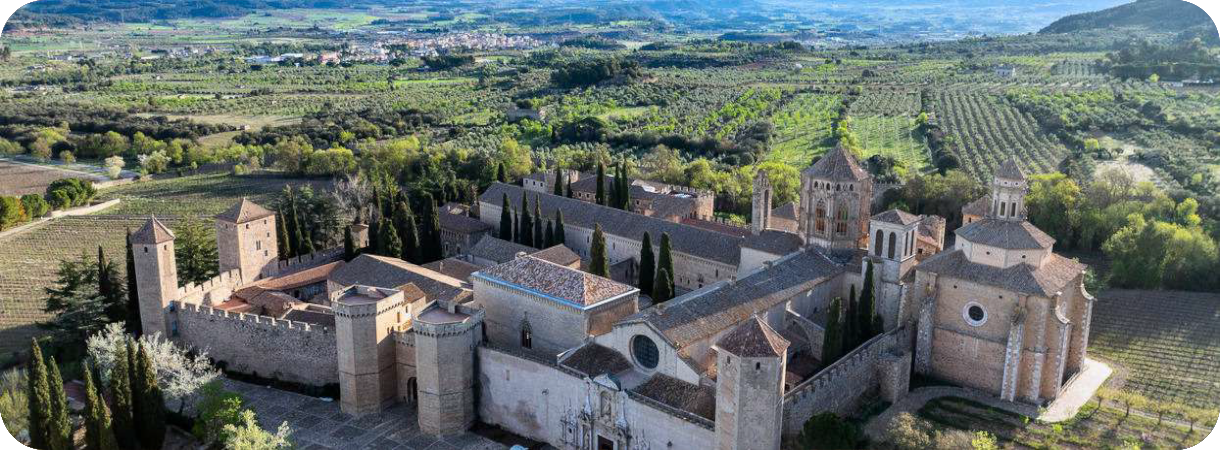 Luchtfoto van het Real Monasterio de Santa María de Poblet, een groot ommuurd middeleeuws kloostercomplex in een groen heuvellandschap in Spanje.