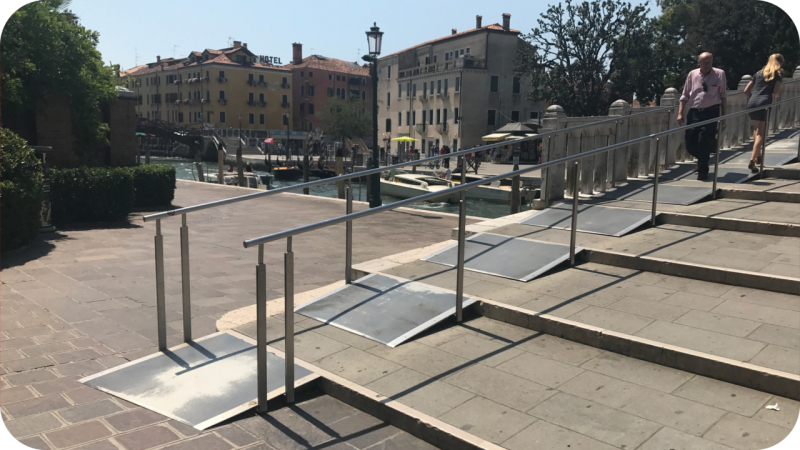 een metalen rolstoel hellingbaan met leuningen over de stenen traptreden van een brug in Venetië