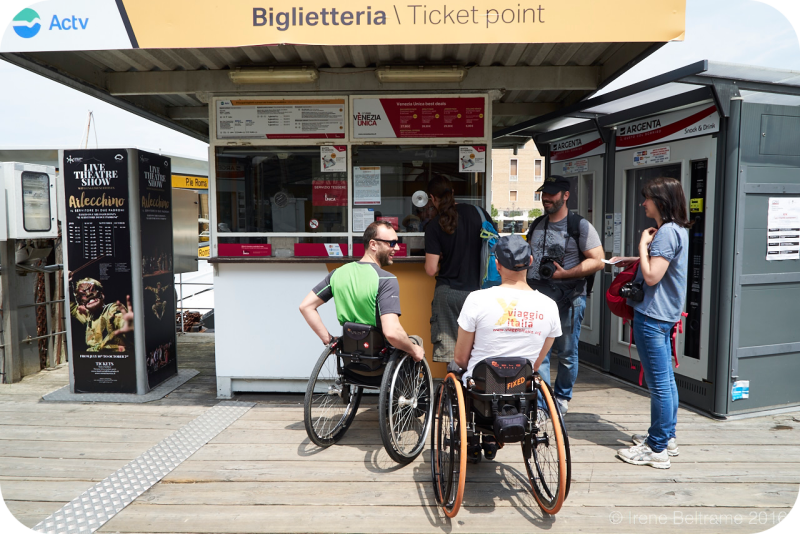 Een ticketloket van het openbaar vervoerbedrijf Actv in Venetië, Italië. Twee rolstoelgebruikers staan bij het loket om kaartjes te kopen