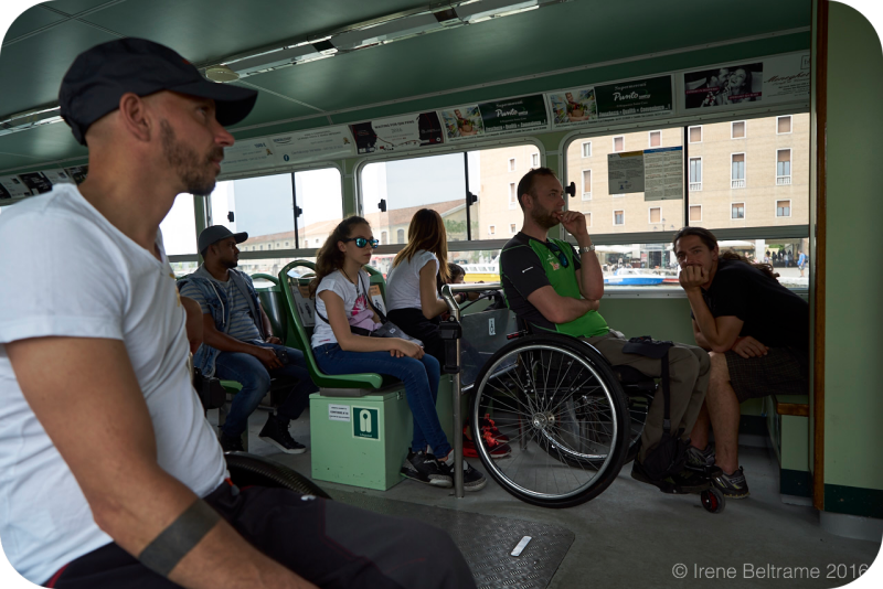 Interieur van een Venetiaanse vaporetto (de bekende openbare waterbus) met passagiers, waaronder een man in een handbewogen rolstoel op een toegankelijke opstelplaats