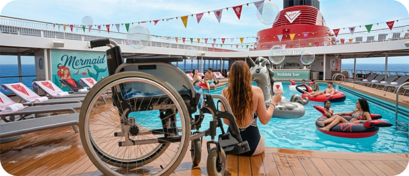 Een rolstoel staat op het houten dek naast een zwembad op een cruiseschip van Virgin Voyages.