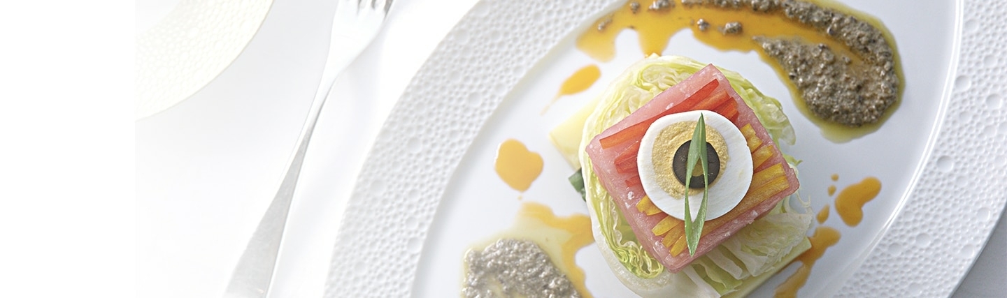 Elegant voorgerecht met sla, tomaat, gekookt ei en olijf, artistiek gepresenteerd met saus en dressing op een fijn bewerkt wit bord.