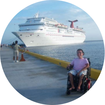 Cory Lee zitten in zijn rolstoel op de kade voor een cruiseschip van Carnival Cruise Line