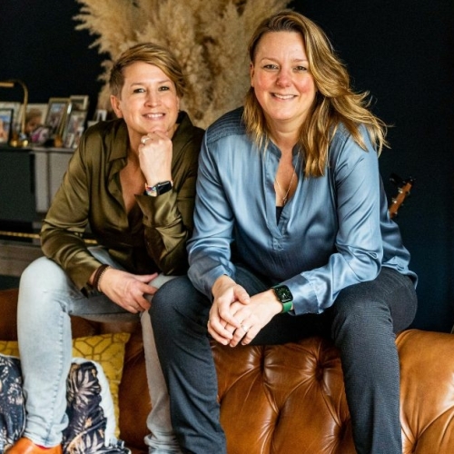 Evelyn & Emilie - Oprichters van Evolve Life Center Evelyn en Emilie Scholtens van Evolve Life Center zitten samen op een leren bank en kijken warm en zelfverzekerd in de camera.