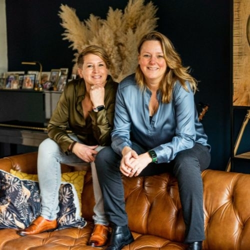 Evelyn en Emilie Scholtens van Evolve Life Center zitten samen op een leren bank en kijken warm en zelfverzekerd in de camera.