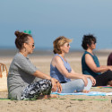 Drie deelnemers mediteren op het strand tijdens yogales