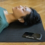 Vrouw ligt op de grond met oortje en telefoon te luisteren naar meditatie