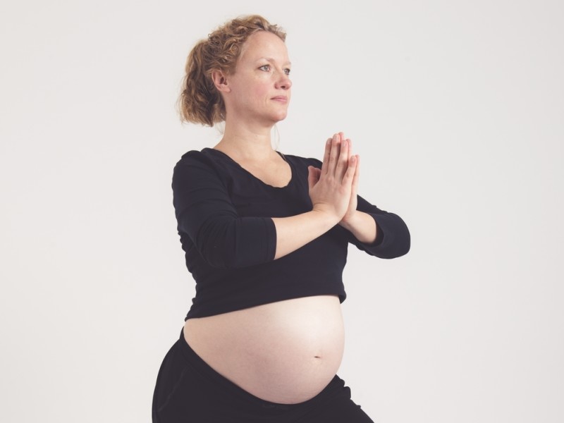 Zwangere vrouw doet namaste warrior pose - krijgerhouding met namaste variatie