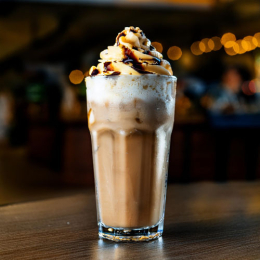 Freddi D'Oro Frozen Cappuccino in een tumblerglas met romige caramelbruine textuur, slagroom en een drizzle van caramel of chocolade.