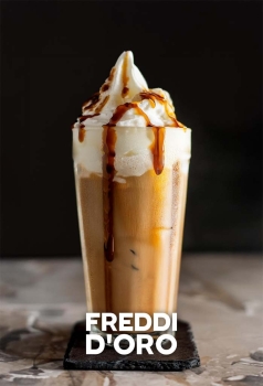 Freddi D'Oro Frozen Cappuccino in een tumblerglas met romige caramelbruine textuur, slagroom en een drizzle van caramel of chocolade.