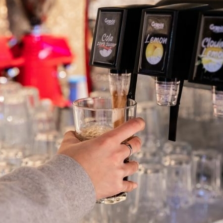 Iemand tapt een glas duurzame Grapos frisdrank uit een postmixmachine.