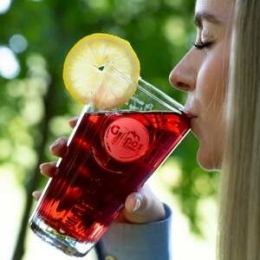 Een mevrouw drinkt uit een glas rode Grapos limonade. Ze vindt het heerlijk!