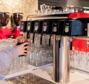 Iemand tapt een cola uit een postmixmachine van Grapos Iemand tapt een glas bruisende cola uit een frisdrankmachine van Grapos Postmix