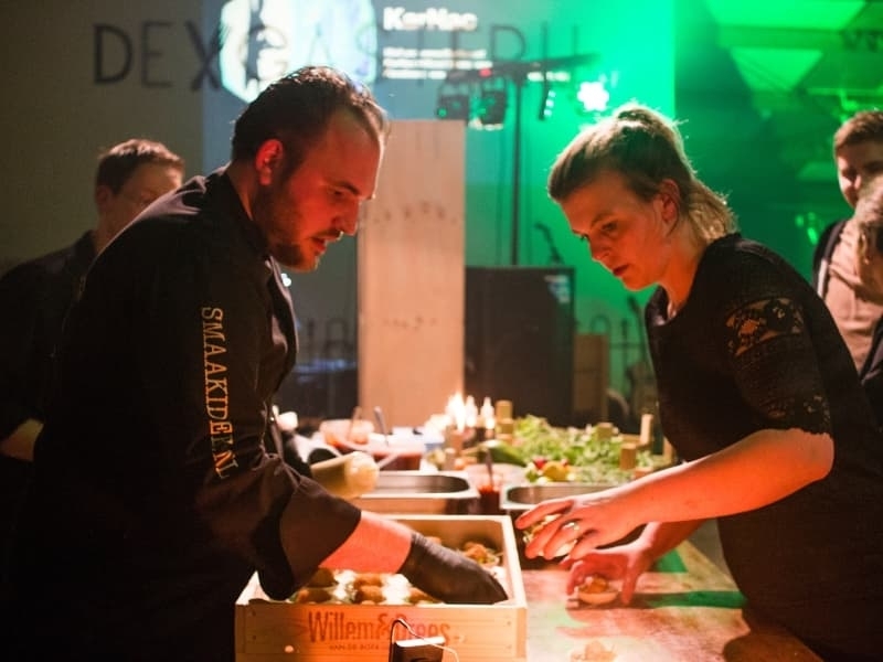 Harold en Lisette bereiden gerechten in de keuken tijdens een druk evenement, teamwork dat de basis vormde voor hun bedrijf