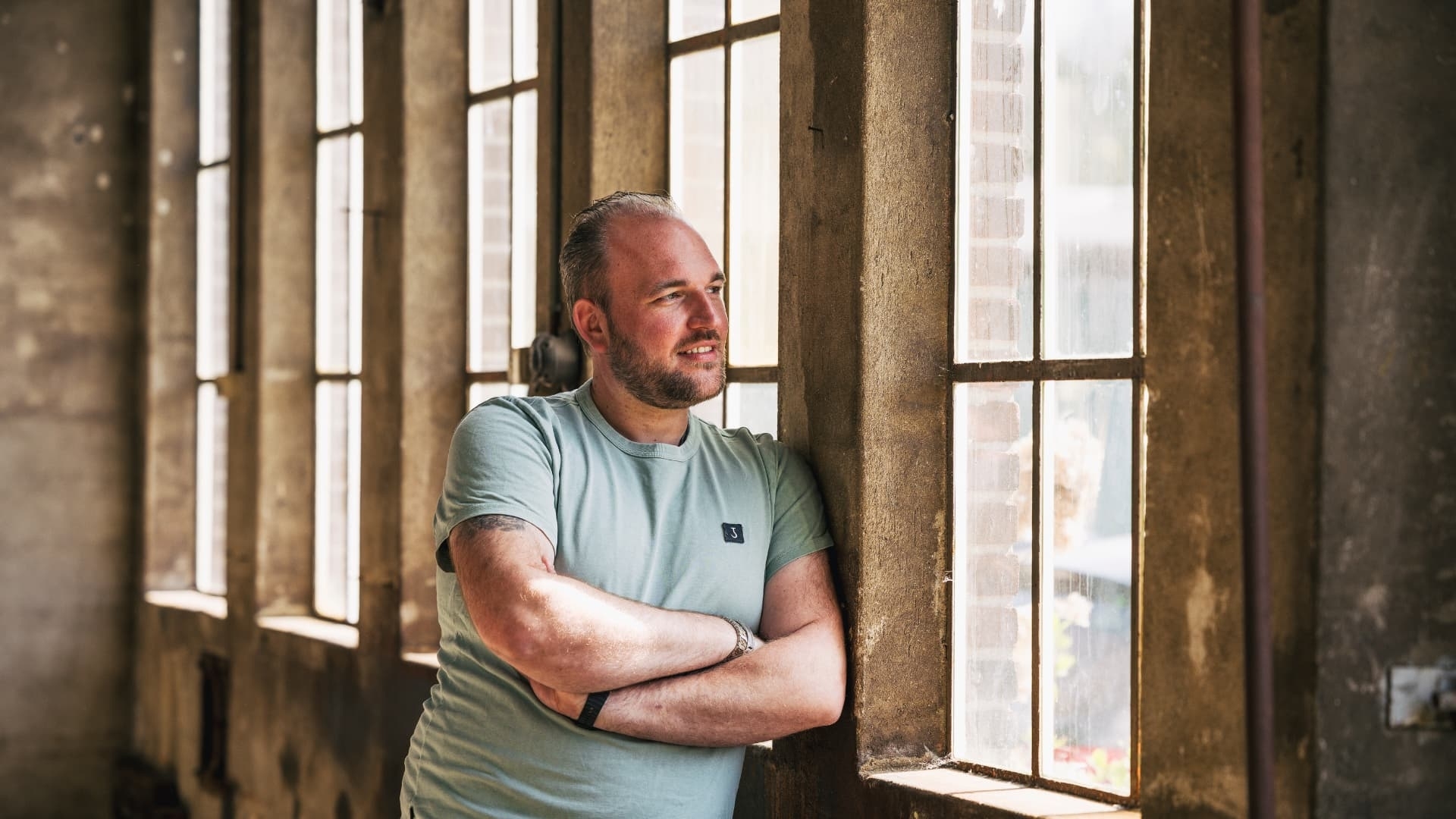 Harold Engelen Grenzeloos Gastvrij Portet van Harold Engelen kijkend uit het raam in een industrieel pand, mede eigenaar van Grenzeloos Gastvrij