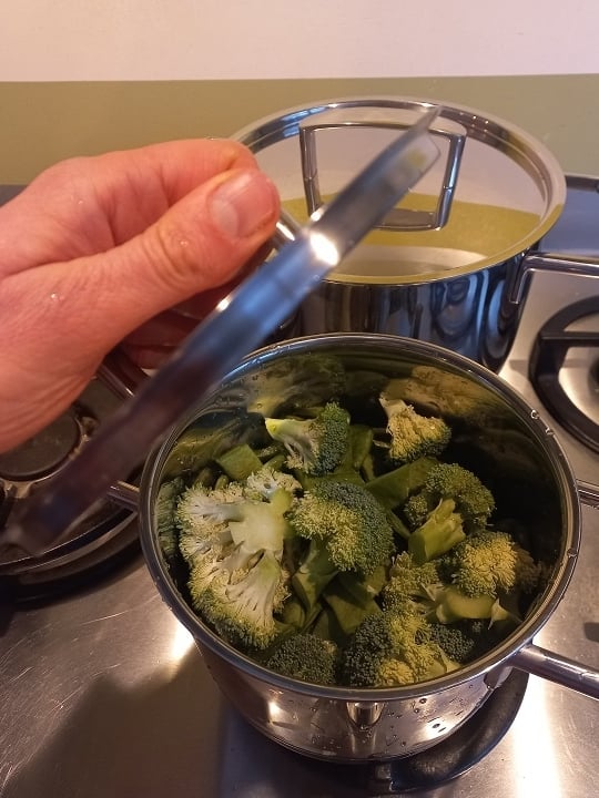 Pannetje met broccoli met een hand die een deksel vasthoudt erboven