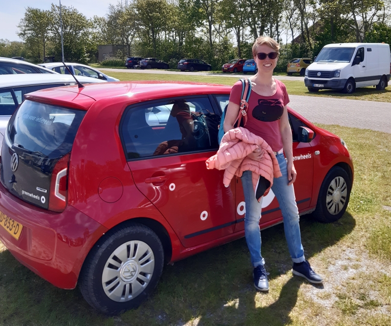 Petra bij een geparkeerde rode Greenwheels auto