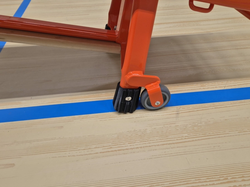 Close-up van het wiel- en remmechanisme van een oranje gymbank op een houten gymzaalvloer