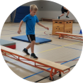 Grote groep kinderen oefent op oranje gymbanken onder begeleiding van gymdocent Kinderen trainen op gekleurde gymbanken in schoolgymzaal met docent