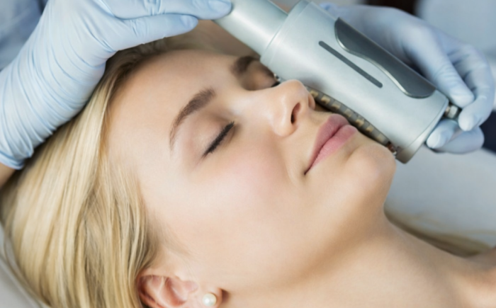 Blonde vrouw ondergaat een rustige, niet-invasieve gezichtsbehandeling met een professioneel huidapparaat in een ontspannen behandelomgeving.