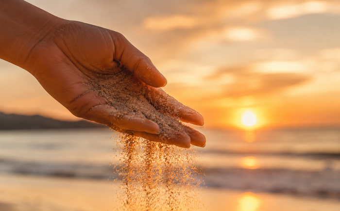 Hand laat zand los op het strand tijdens zonsondergang als symbool voor loslaten.