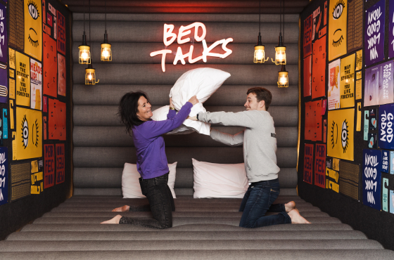 Collega's Femke en Thom slaan elkaar met kussens op een groot bed.