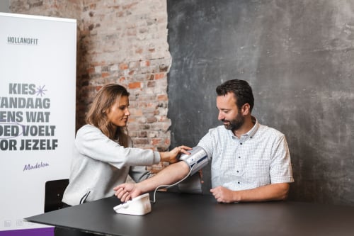 Een adviseur doet een band om de bovenarm van de healthcheck deelnemer om zo zijn hartslag te meten