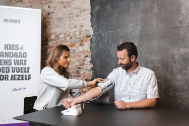 Een adviseur doet een band om de bovenarm van de healthcheck deelnemer om zo zijn hartslag te meten