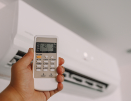 Een hand houdt een afstandsbediening voor een airco, ingesteld op 18 graden. De afbeelding laat zien hoe airconditioning zorgt voor een aangenaam en gecontroleerd binnenklimaat.