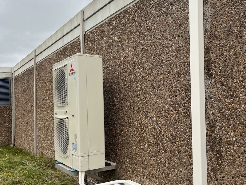 Zakelijke airco-buitenunit van Mitsubishi Electric tegen een bedrijfsmuur met strak leidingwerk.