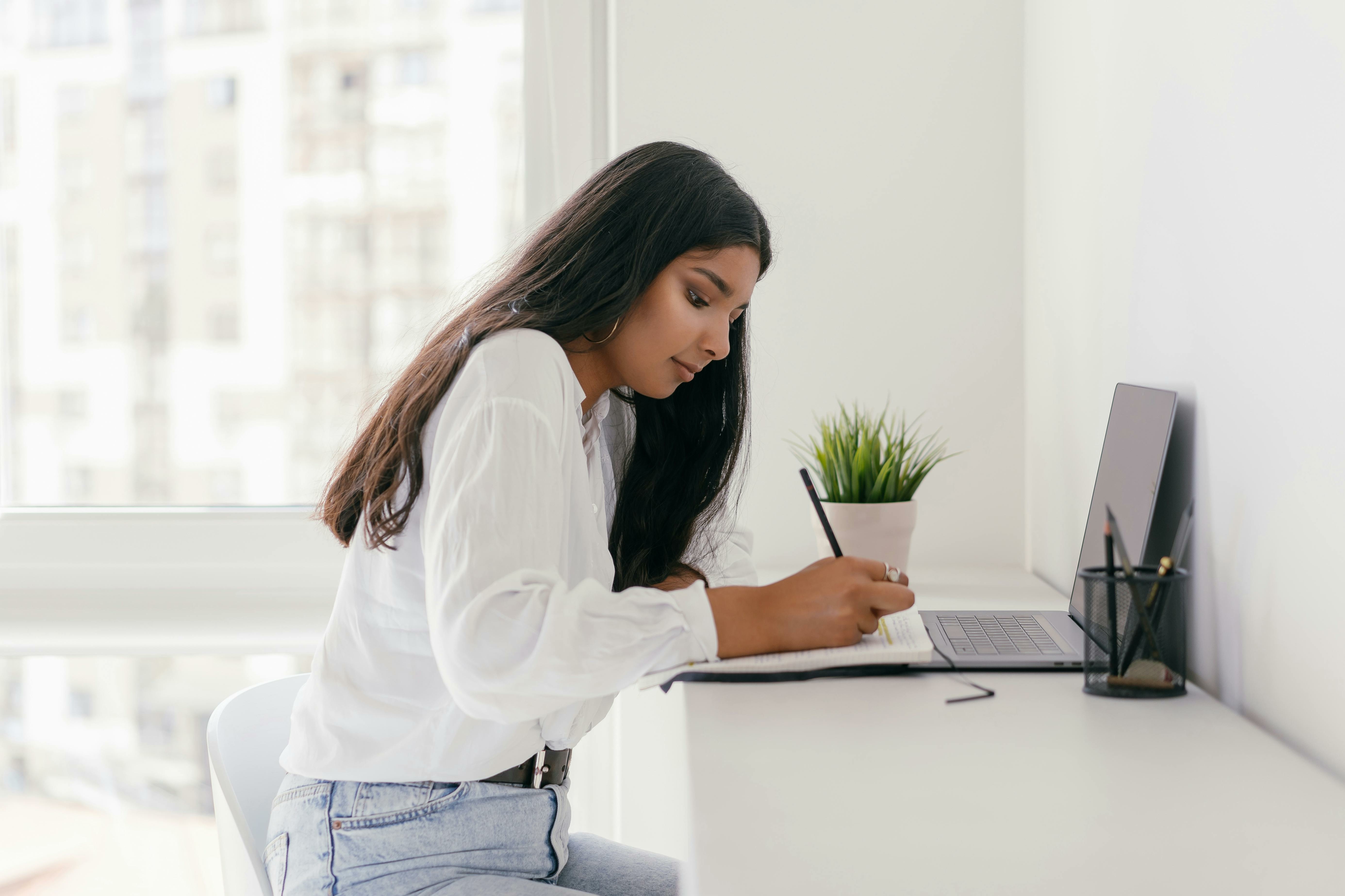 Vrouw zit achter bureau en schrijft iets op