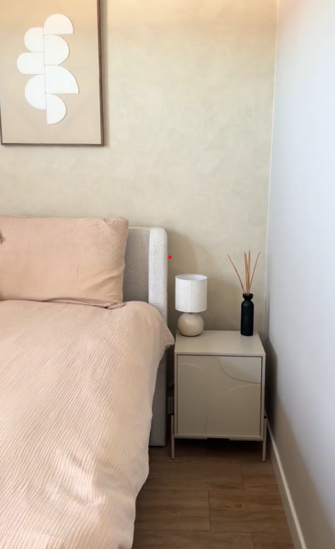 Beige Action nachtkastje naast bed in rustige slaapkamer met warme neutrale kleuren