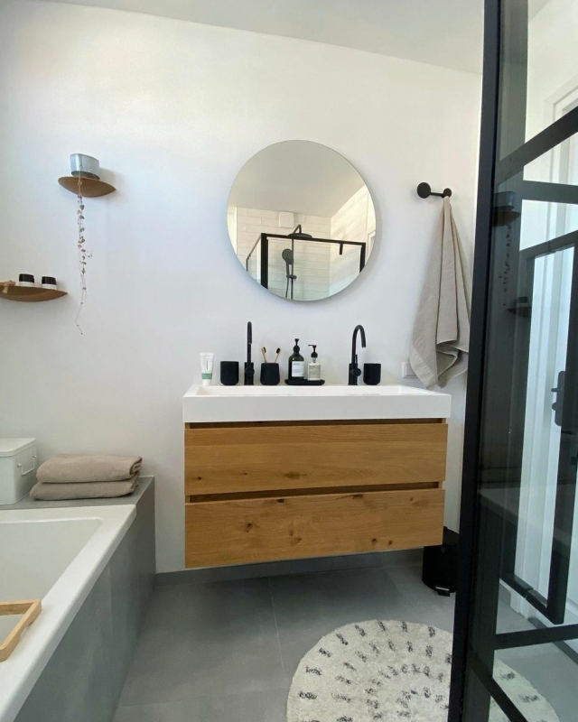 een lichte moderne badkamer met houten wastafelmeubel en glazen douchedeuren