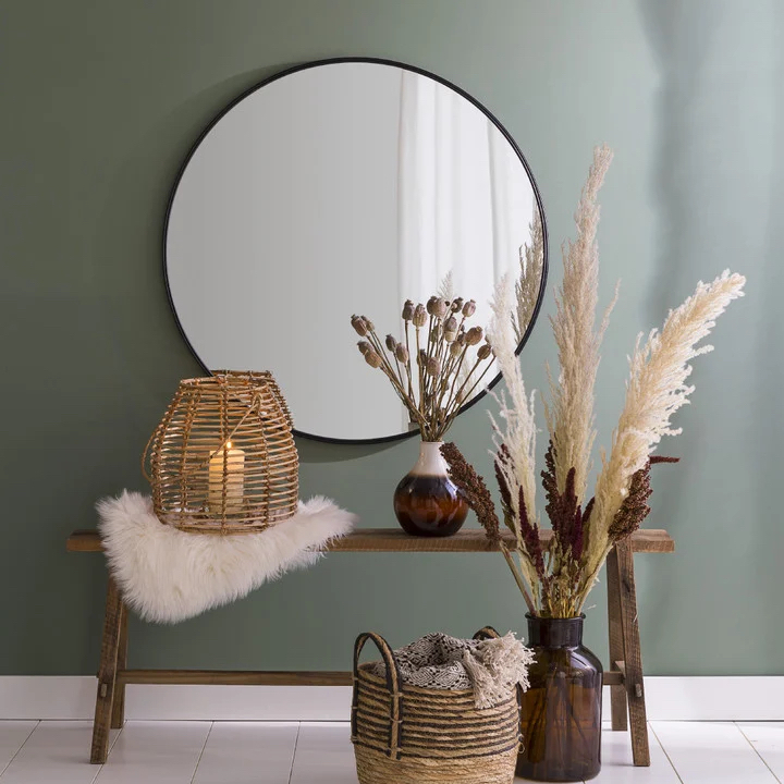een ronde spiegel met zwart frame hangt aan een groene muur met accessoires eromheen