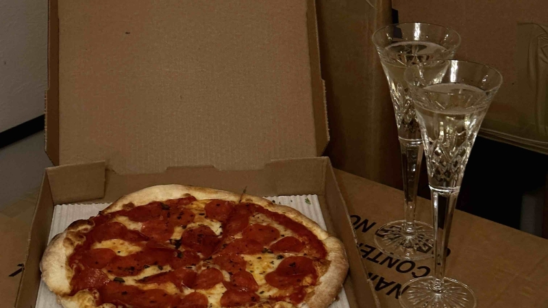 op een verhuisdoos staan twee glazen champagne en een doos met pizza