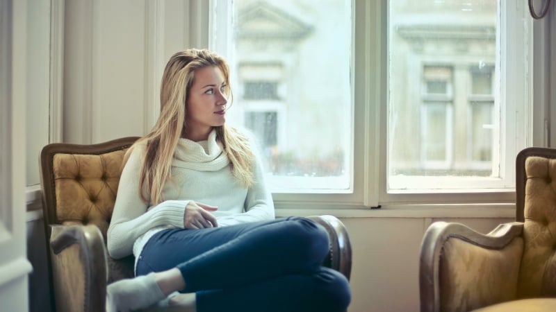 vrouw zit bij raam in woonkamer