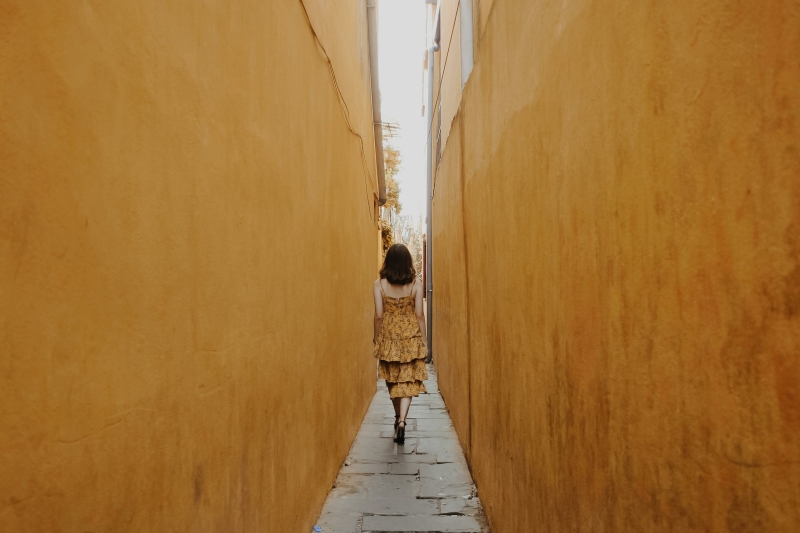 vrouw in gele jurk loopt door smal straatje